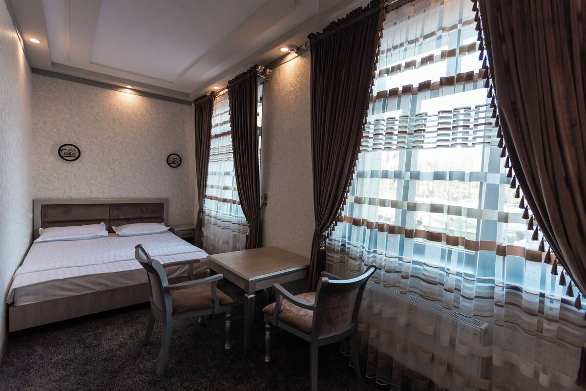 A hotel room with a bed, a table, two chairs, and curtains.