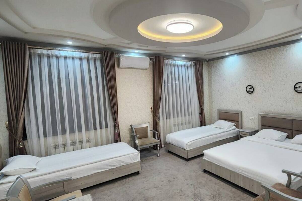 A hotel room with three single beds, a chair, a desk, and a ceiling light fixture.
