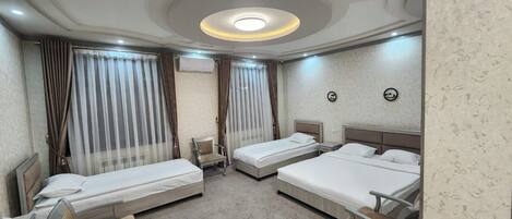 A hotel room with three single beds, a chair, a desk, and a ceiling light fixture.