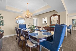 A dining area with a round table, blue upholstered chairs, and a chandelier. - Oceanfront 5 Bdrm 17th Flr Beach or Golf Outings (North Myrtle Beach)