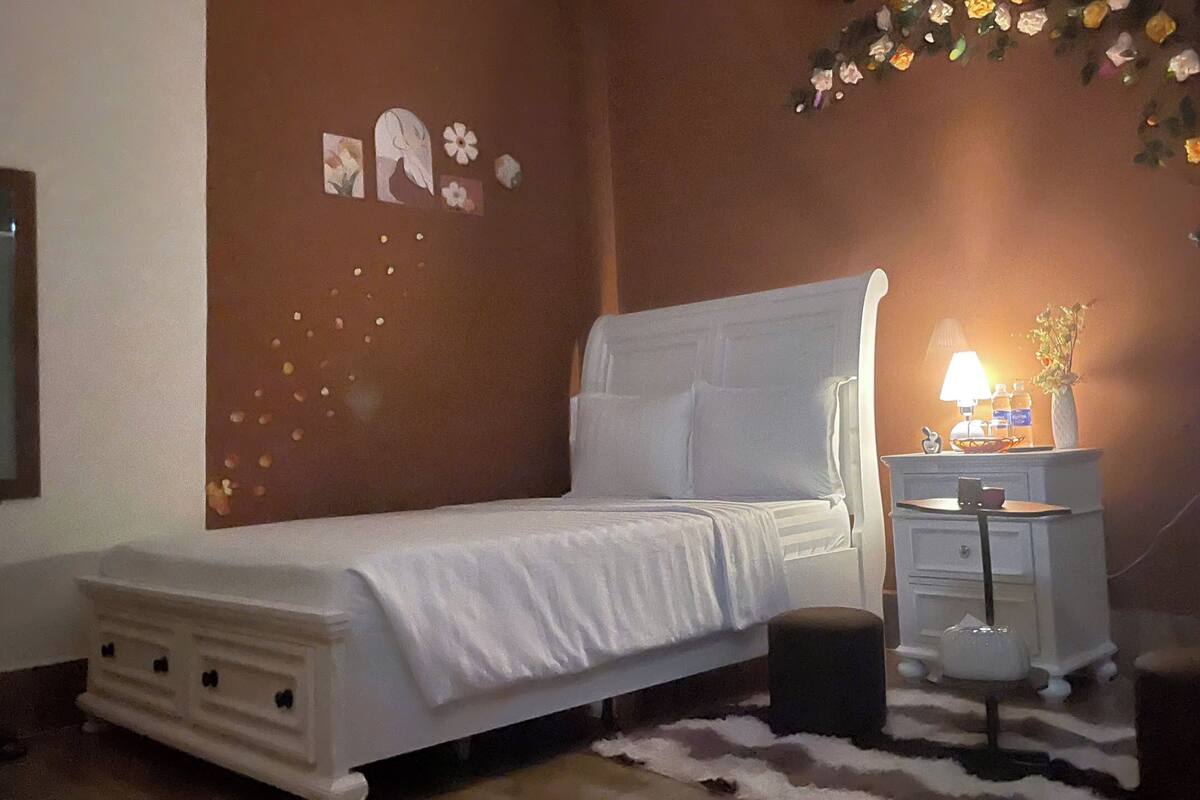 Un dormitorio con cama, mesita de noche, lámpara y decoración mural.