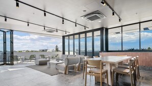 A modern rooftop lounge with a large table and chairs, a sofa, and a view of the city skyline. - Bright Studio With Rooftop BBQ in Fremantle (Perth)