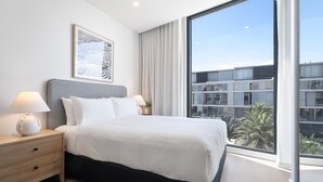 A modern hotel room with a large bed, bedside lamps, a framed artwork, and a view of the city through floor-to-ceiling windows. - Bright Studio With Rooftop BBQ in Fremantle (Perth)