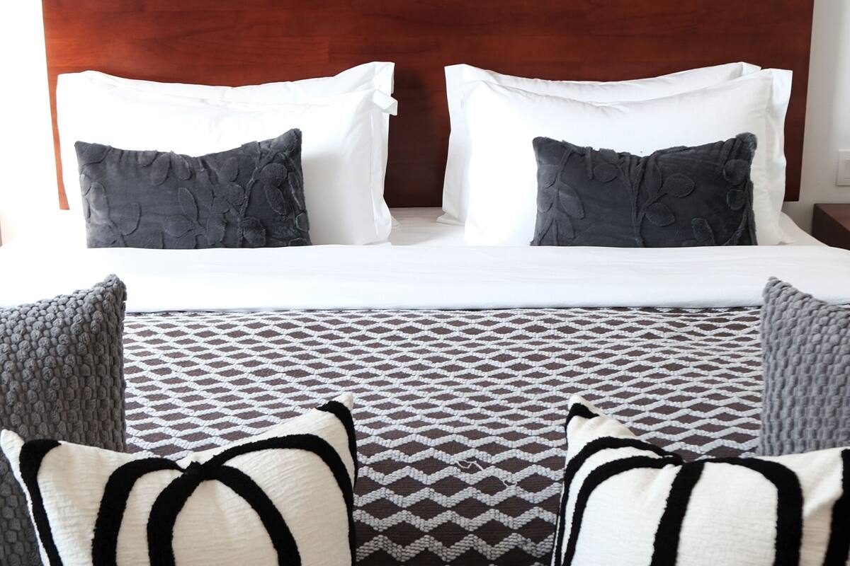 A neatly arranged bed with a checkered floor, a patterned throw, and two pillows with a black and white design.