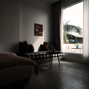 A hotel room with a bed, a sofa, a small table, and a window with a view of palm trees. - Serenity Home (Siem Reap)