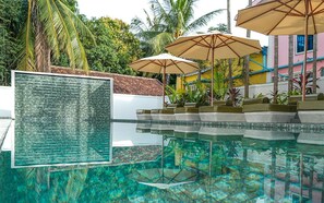 A clear pool with a glass panel displaying text, surrounded by palm trees and umbrellas. - Serenity Home (Siem Reap)