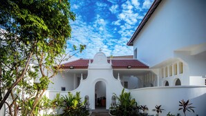 A white building with a red-tiled roof, a central archway, and a courtyard with plants and statues. - Serenity Home (Siem Reap)