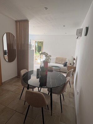 A dining area with a round glass table, four chairs, a potted plant, and a sofa in the background. - Charming two-bedroom apartment with a garden   (Saint-Julien)