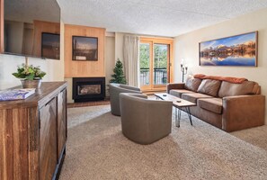 A living room with a fireplace, leather sofa, and a large window with a view. - Best in Breck. Ski in, ski out. Pool and hot tubs. (Breckenridge)
