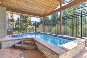 Ein Schwimmbecken im Freien mit Steinrand, Stufen zum Ein- und Ausstieg und einem Metallzaun, der das Becken umgibt.