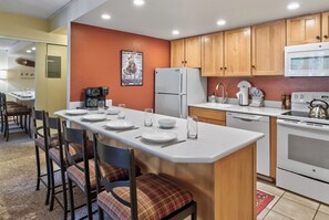 A modern kitchen with a central island, wooden cabinets, and a dining area with chairs. - Best in Breck. Ski in, ski out. Pool and hot tubs. (Breckenridge)