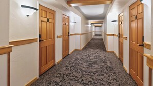 A hotel hallway with wooden doors, white walls, and a patterned carpet. - Best in Breck. Ski in, ski out. Pool and hot tubs. (Breckenridge)