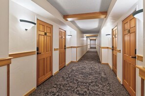 Ein Hotelgang mit Holztüren, weißen Wänden und einem gemusterten Teppich.