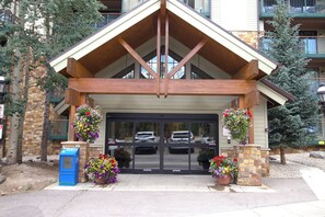 A building entrance with a wooden gable roof, stone pillars, and flower baskets. - Best in Breck. Ski in, ski out. Pool and hot tubs. (Breckenridge)
