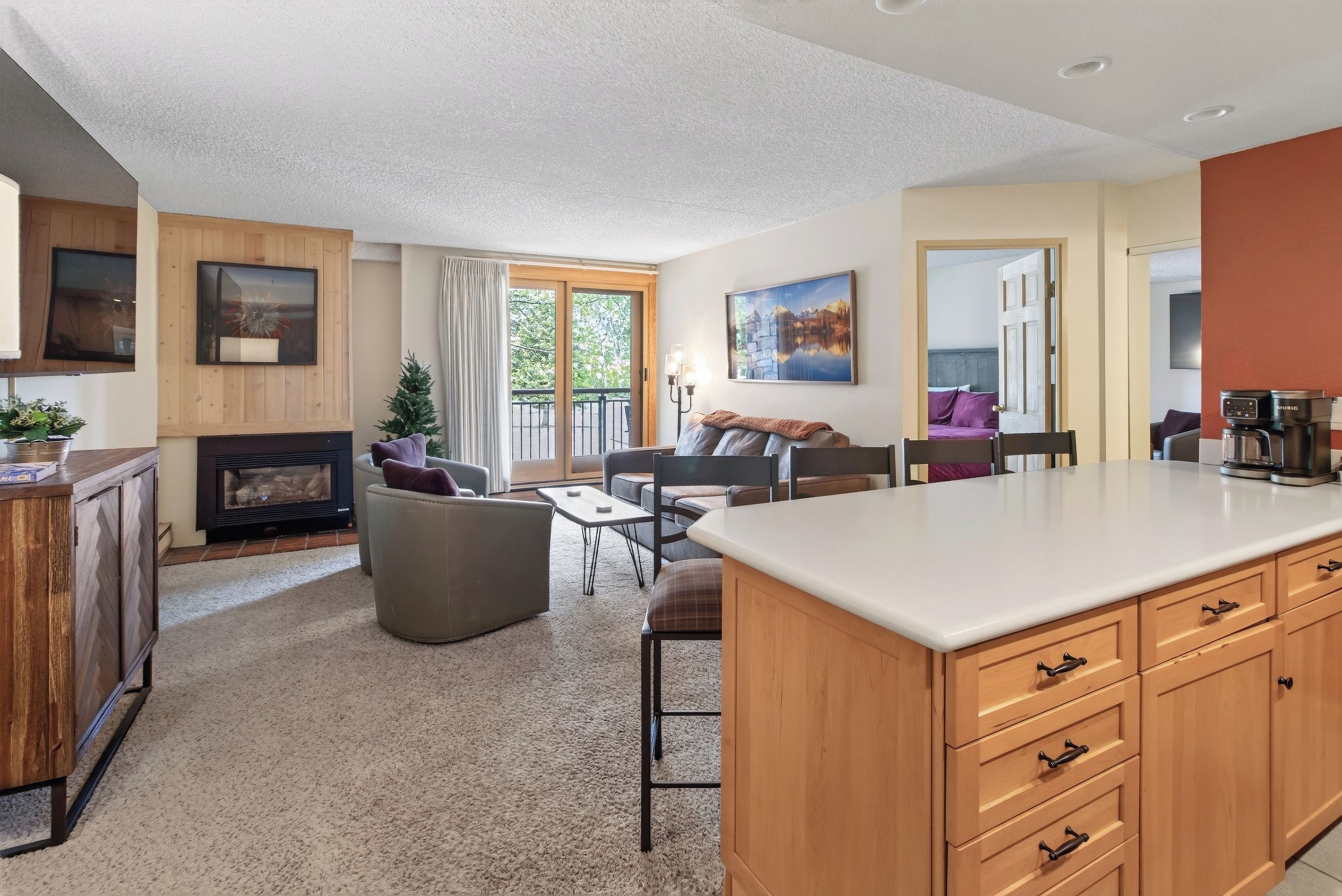 A modern living room with a fireplace, seating area, and a kitchen with a large island.