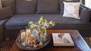 A modern living room with a dark grey sofa, a wooden coffee table with a tray of snacks and candles, and a large abstract painting on the wall. - Tzivaeri, Lovely village house with ample outdoor area and plunge pool. (Chania)