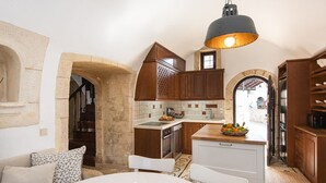 A cozy kitchen with wooden cabinets, a stone archway, and a dining area with a table set for breakfast. - Tzivaeri, Lovely village house with ample outdoor area and plunge pool. (Chania)