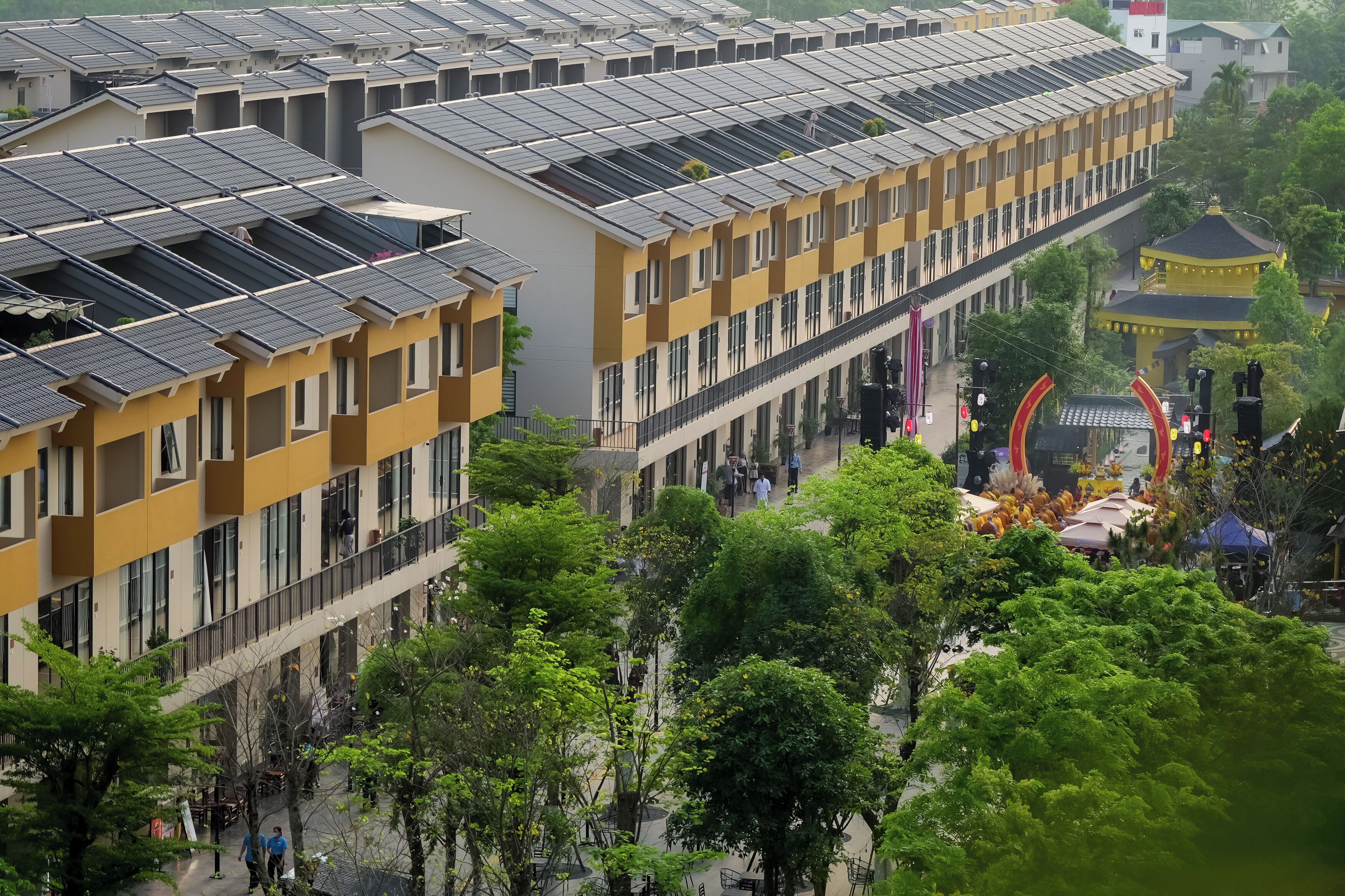 Un immeuble à plusieurs étages doté de panneaux solaires sur le toit, une cour intérieure avec des arbres et un bâtiment traditionnel surmonté d’un toit doré.