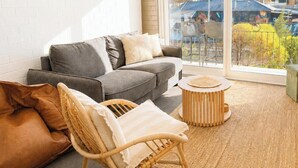 Uma sala de estar com um sofá cinzento, uma poltrona de vime e uma mesa de madeira redonda.