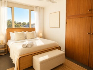 A bedroom with a wooden bed, a bench, a nightstand, and a wardrobe. - South Beach Sands - close to the beach (South Fremantle)