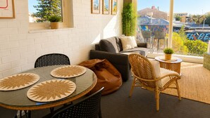 Uma sala de estar moderna com uma mesa de vidro, um sofá, uma poltrona de vime e uma varanda com vista para a cidade.