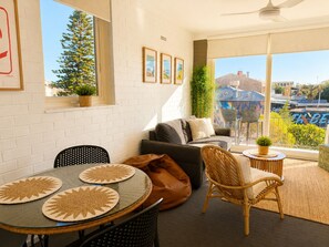 A modern living room with a glass table, a sofa, a wicker chair, and a balcony with a view of the city. - South Beach Sands - close to the beach (South Fremantle)
