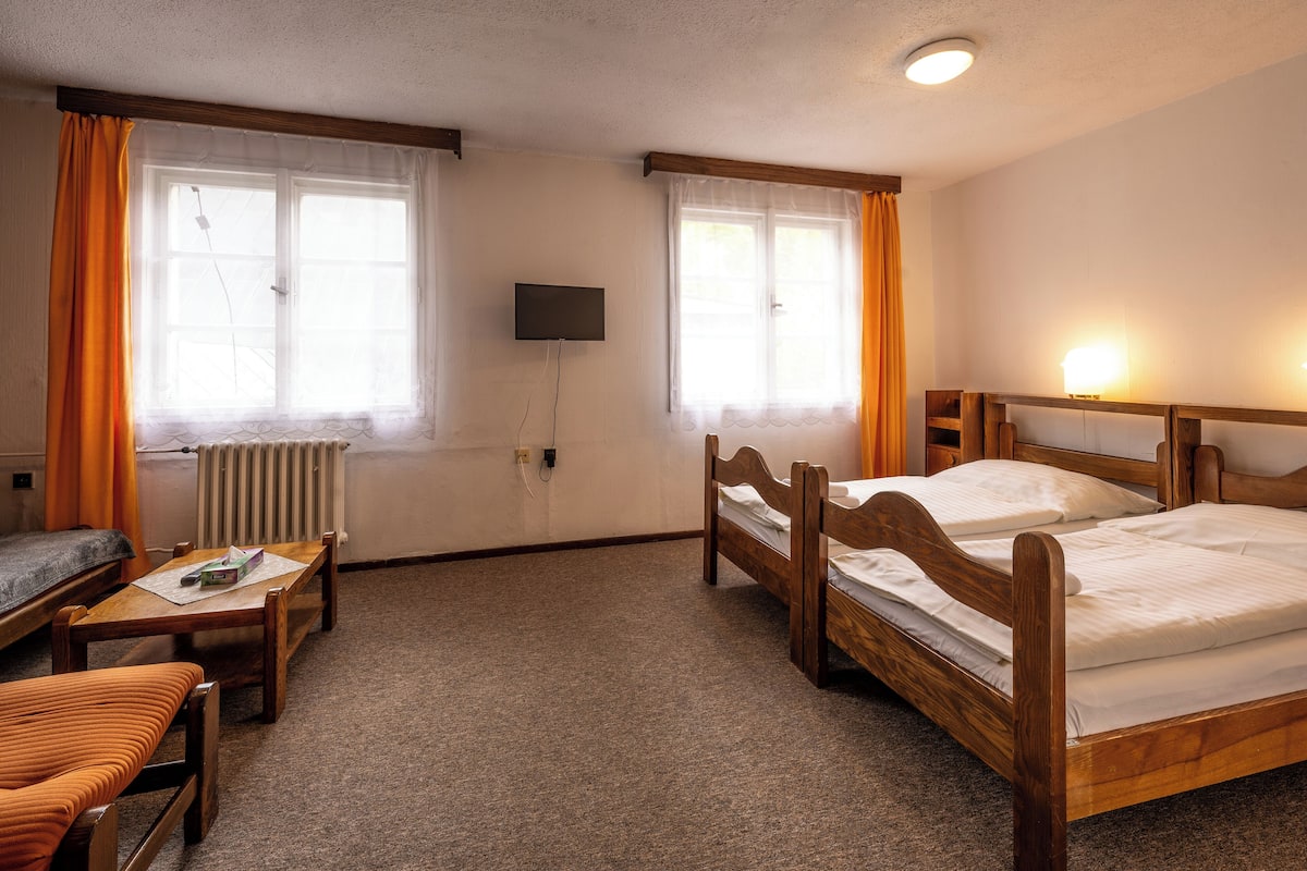 A hotel room with two wooden beds, a small table, a chair, a sofa, and a TV mounted on the wall.