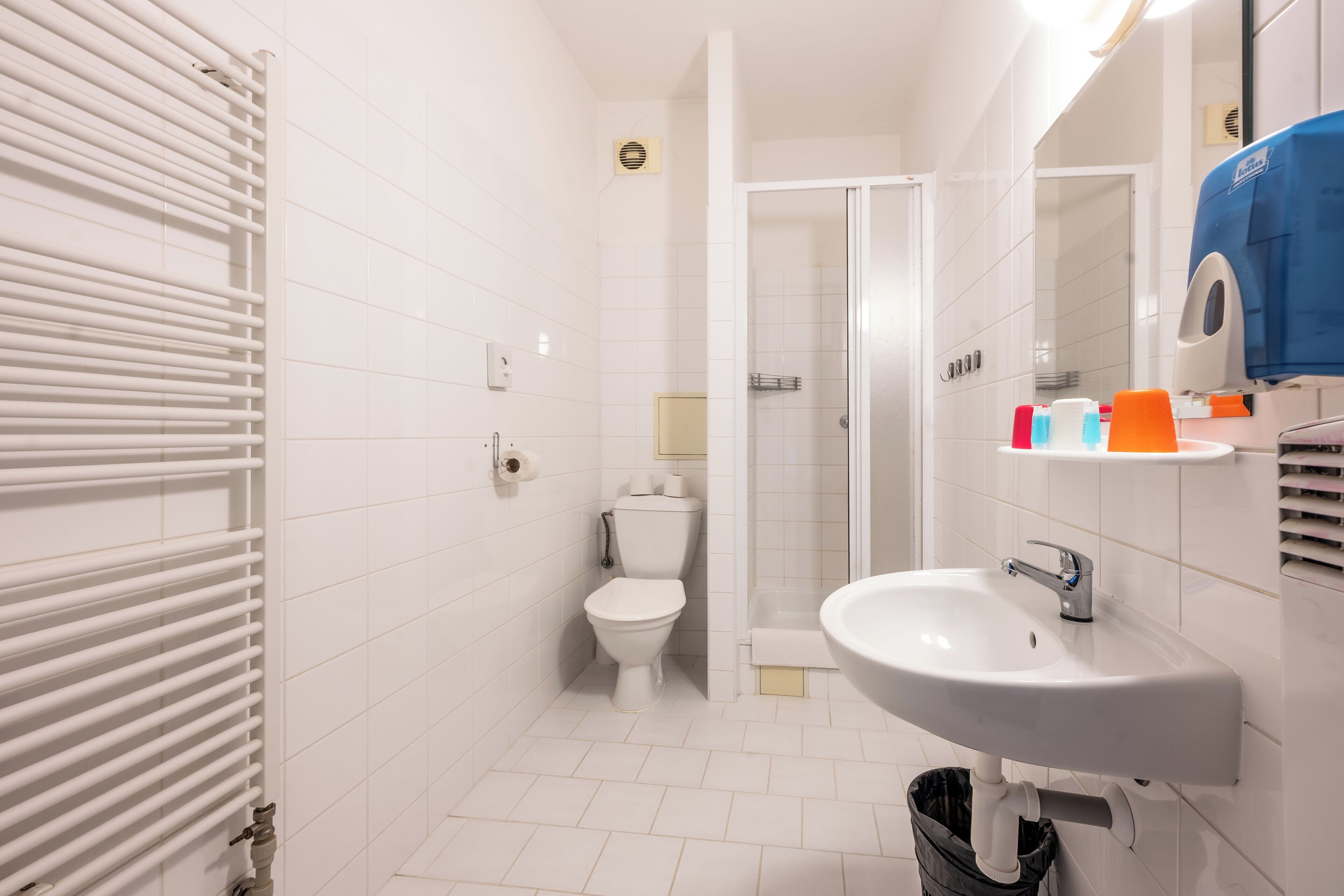 A modern bathroom with a white tiled floor, a toilet, a sink, and a shower.
