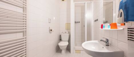 A modern bathroom with a white tiled floor, a toilet, a sink, and a shower.