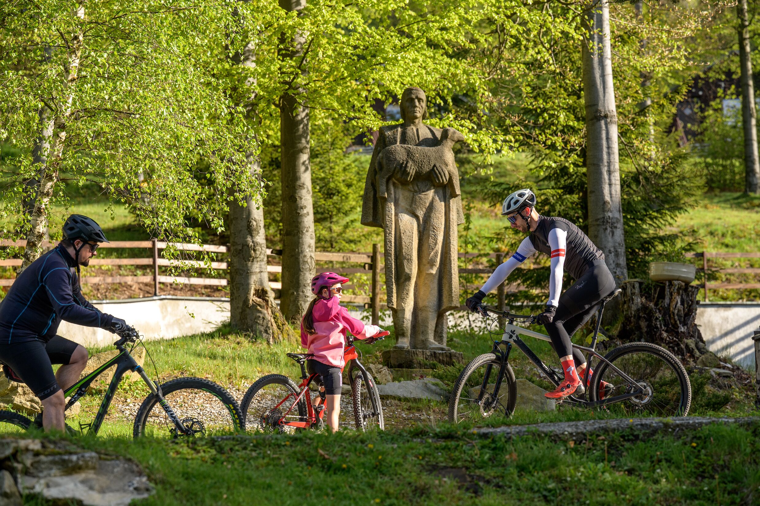Un parque con una estatua, una cerca de madera y un camino para bicicletas.