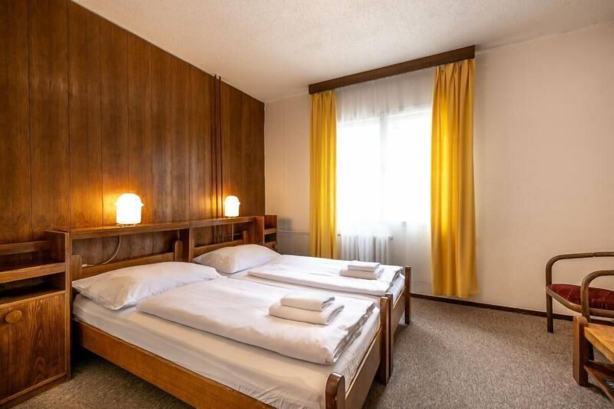 A hotel room with two wooden beds, a wooden headboard, a small wooden desk, and a chair.