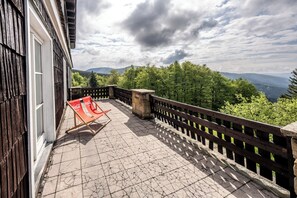 A balcony with a Coca-Cola branded chair, a stone planter, and a wooden railing overlooking a forested landscape. - Hotel Tanečnica (Prostredni Becva)