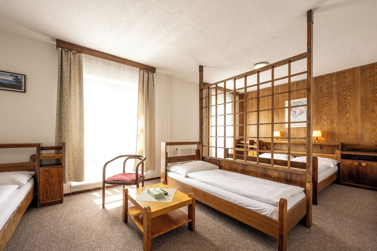 A room with two wooden beds, a wooden desk, a chair, and a large window with curtains.