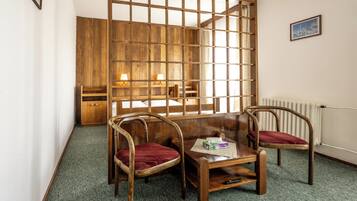 Une pièce avec une cloison en bois, deux chaises en bois dotées de coussins rouges, une petite table en bois sur laquelle se trouvent une boîte et une télécommande, et un radiateur fixé au mur.
