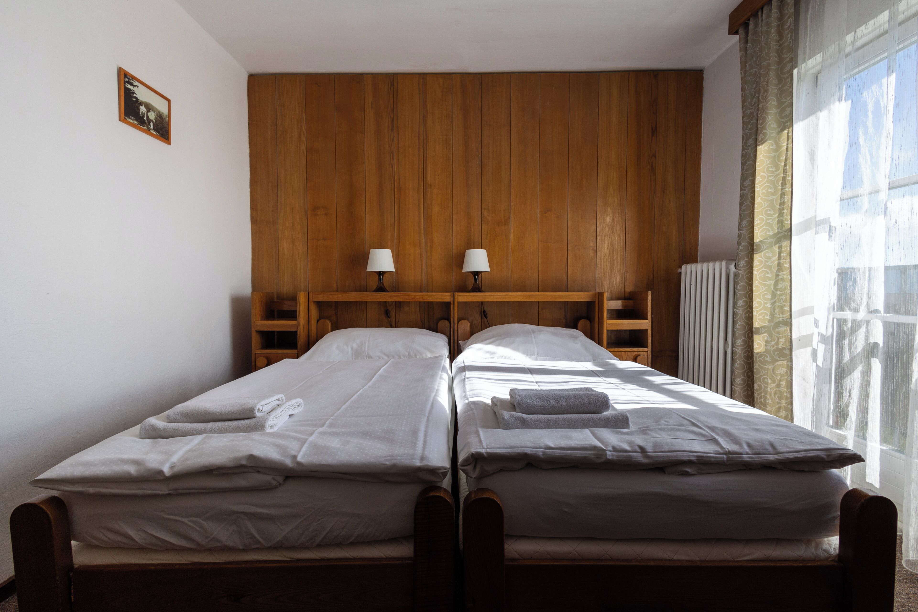 A twin room with two single beds, wooden headboard, bedside lamps, and a window with curtains.