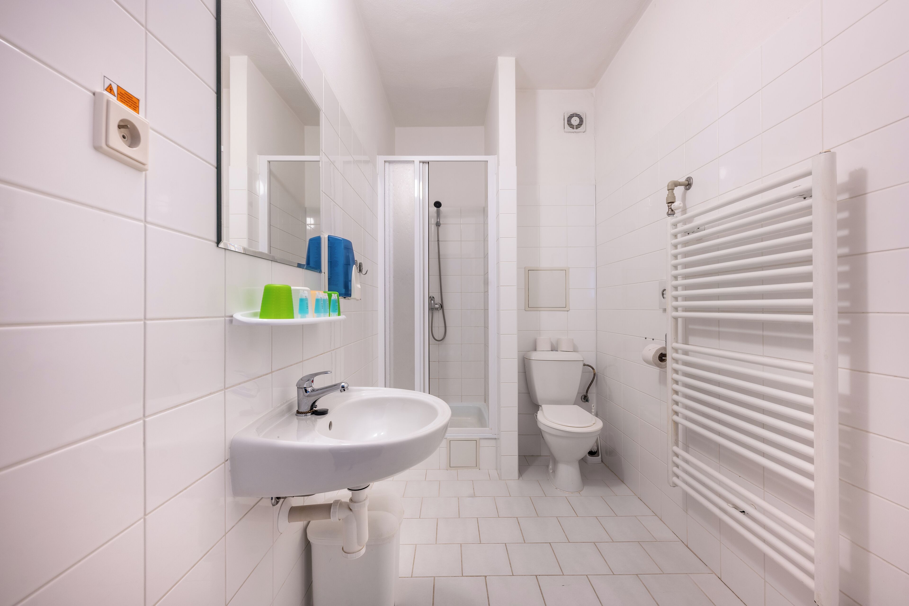 A modern bathroom with a white sink, toilet, and shower. There is a towel rack and a mirror above the sink.