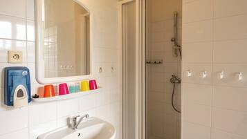 Ein Badezimmer mit einem weißen Waschbecken, einem Spiegel, einer Dusche und einem Regal mit bunten Tassen.