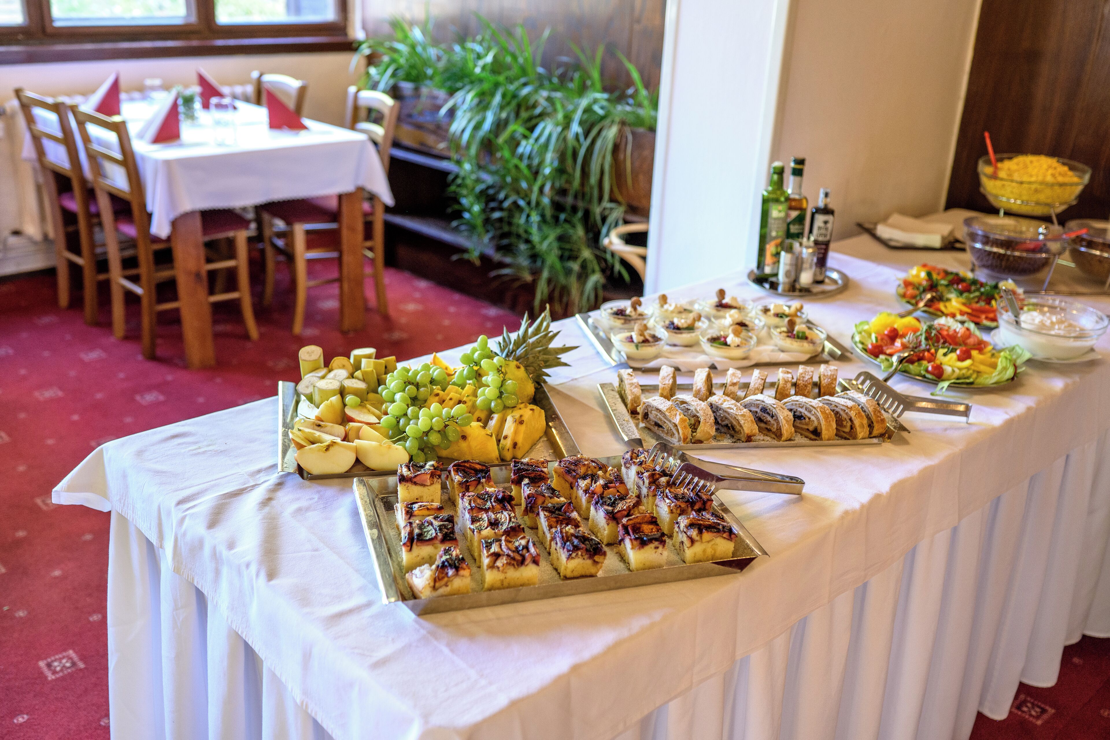 A buffet table with various food items, including fruits, pastries, and salads.