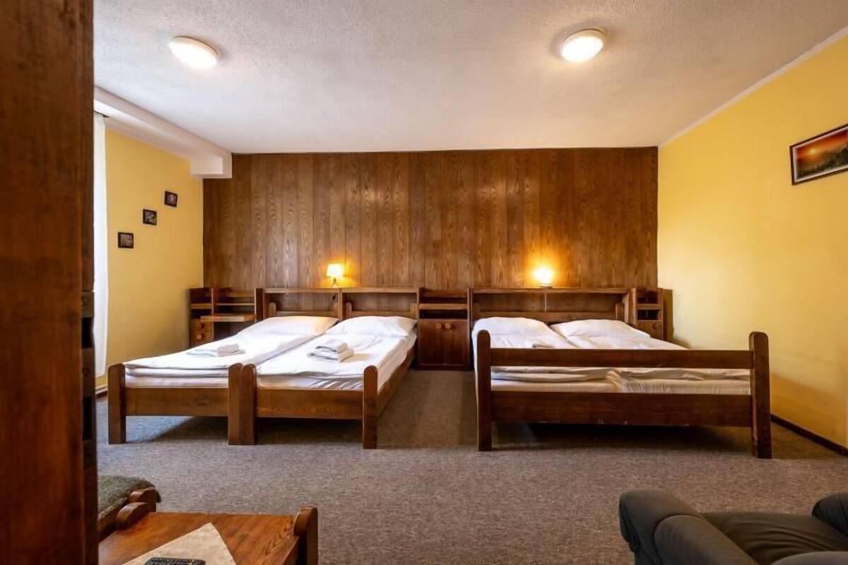 A room with two wooden beds, a small table, and a wall-mounted shelf.