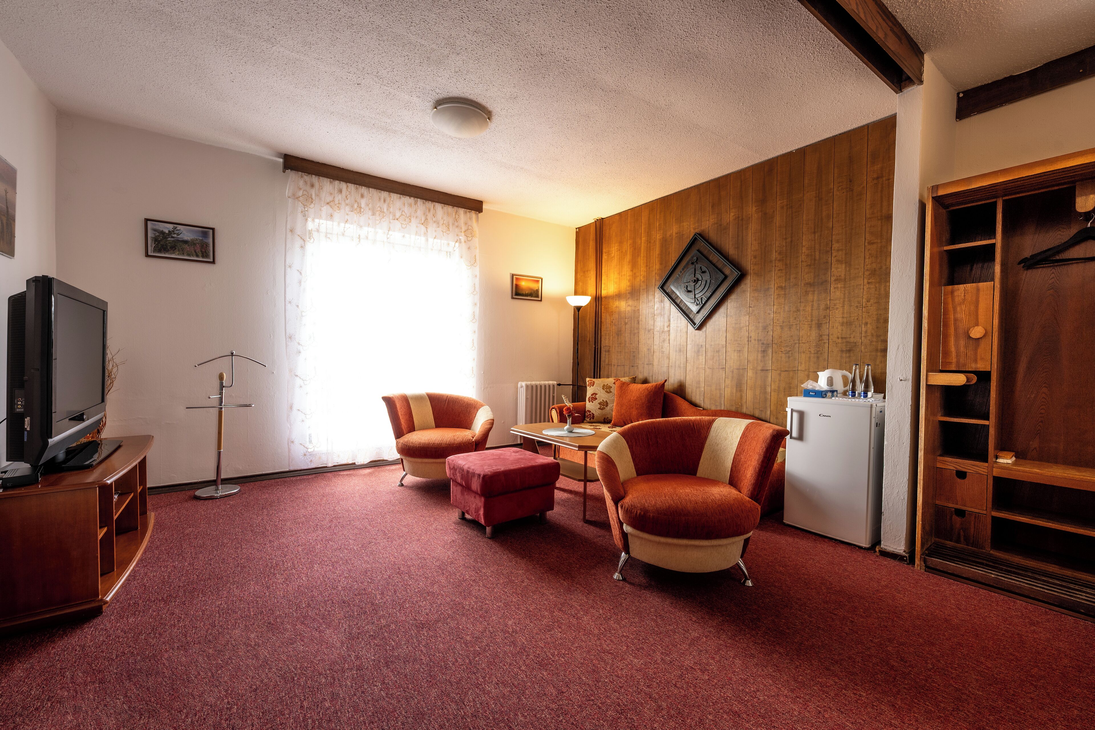 A living room with a red carpet, wooden paneling, a television, a sofa, and a small table.