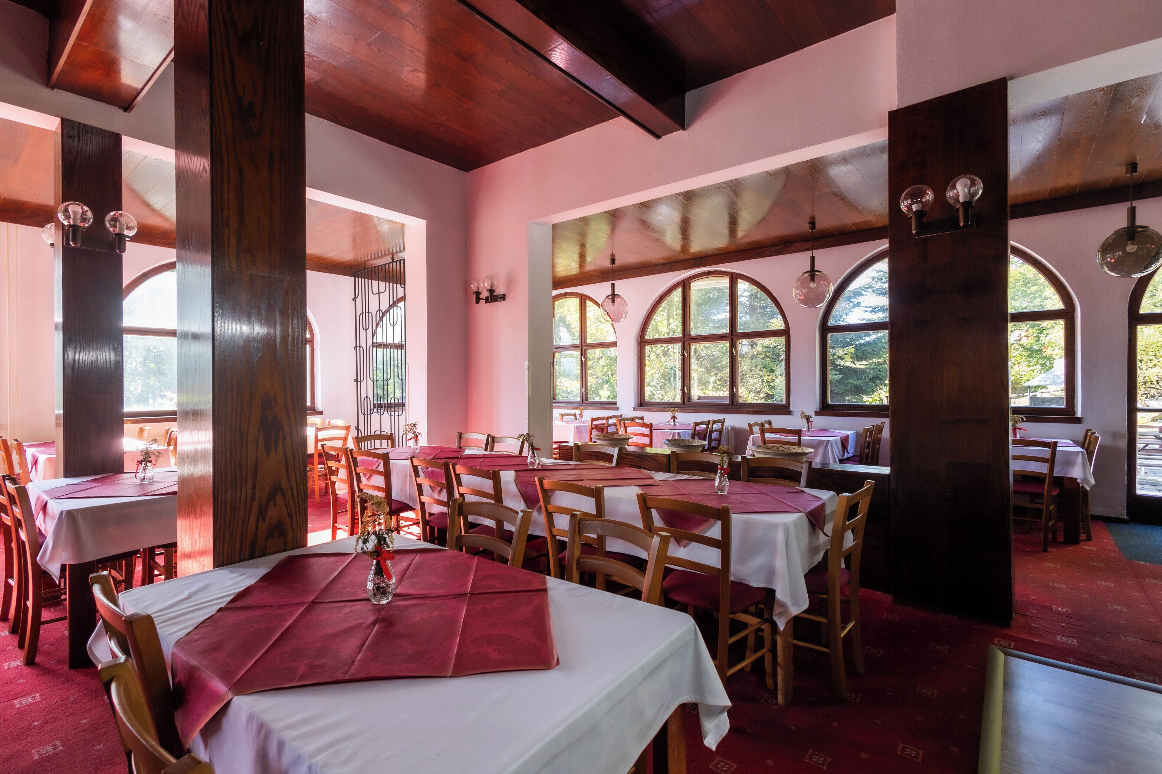 Un restaurant avec des poutres en bois, des fenêtres en arc de cercle et des tables dressées avec des nappes blanches et des serviettes rouges.