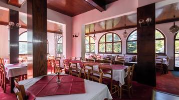 Un restaurant avec des poutres en bois, des fenêtres en arc de cercle et des tables dressées avec des nappes blanches et des serviettes rouges.