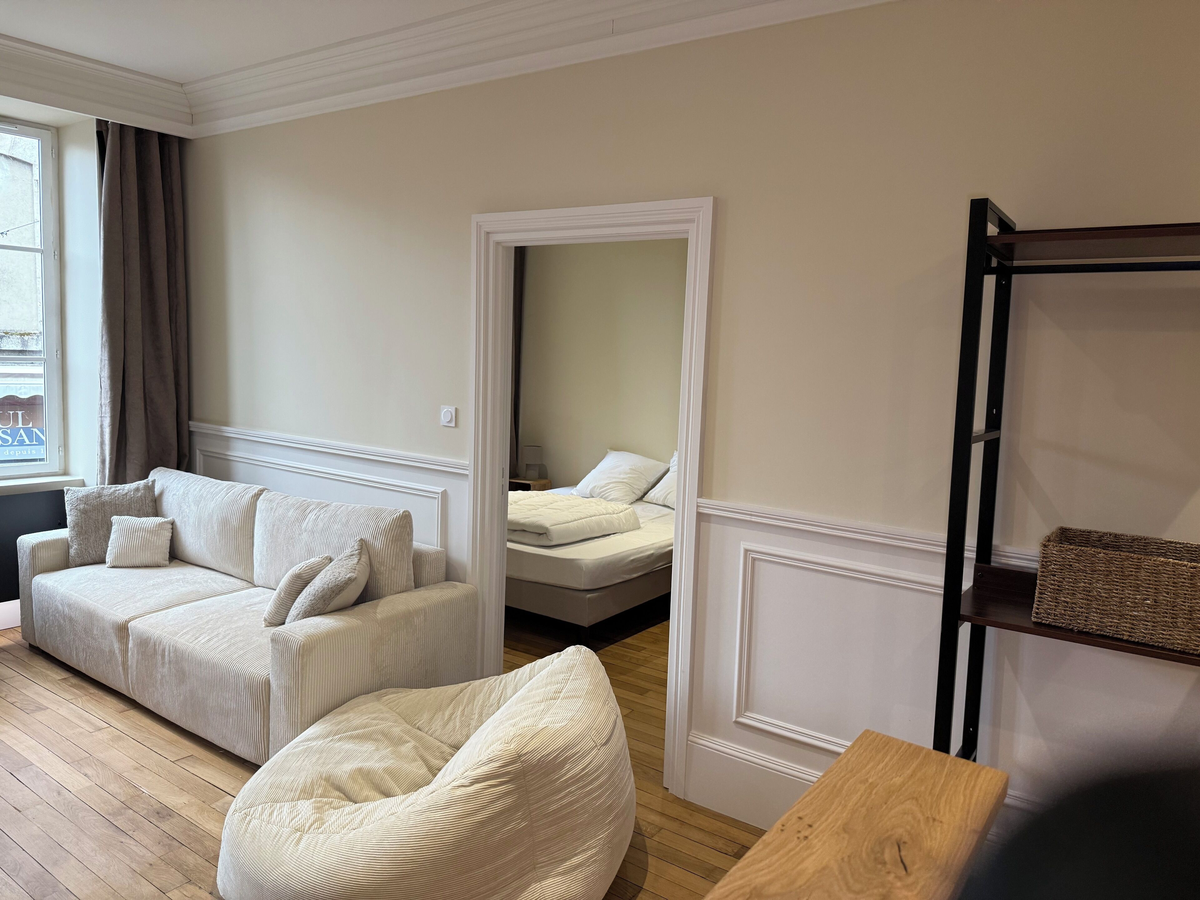 Ein Zimmer mit einem beige gefärbten Sofa, einem Holztisch und einem Bett mit weißer Bettwäsche.