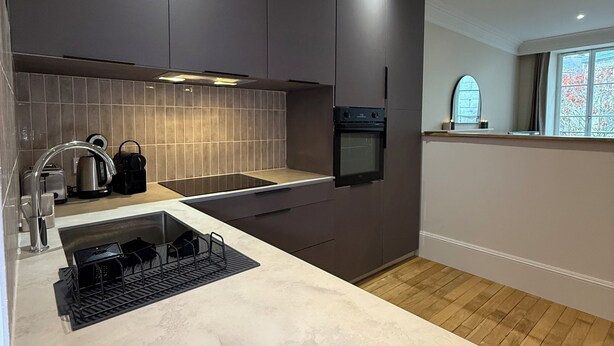 A modern kitchen with dark cabinetry, a stainless steel sink, and a built-in oven. - The Haussman Suite (Guéret)