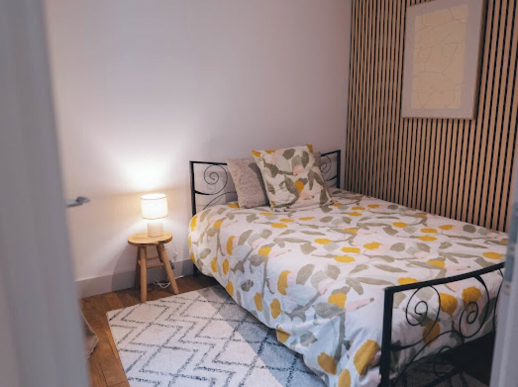 Une chambre à coucher avec un lit, une table de chevet avec une lampe, un tapis à motifs et un mur orné de lignes verticales.