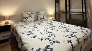A bedroom with a bed, two bedside tables, a wall-mounted shelf, and a bunk bed. - The Haussman Suite (Guéret)