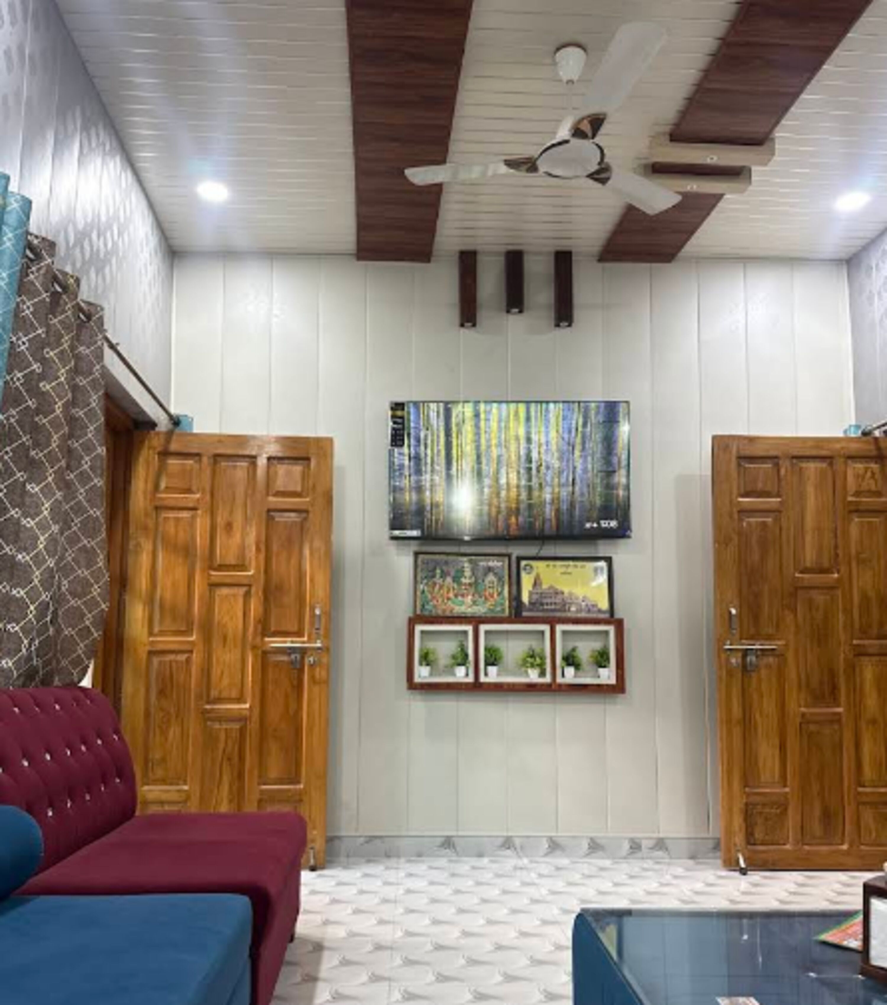 A room with a ceiling fan, wooden wardrobes, a sofa, and a TV mounted on the wall.
