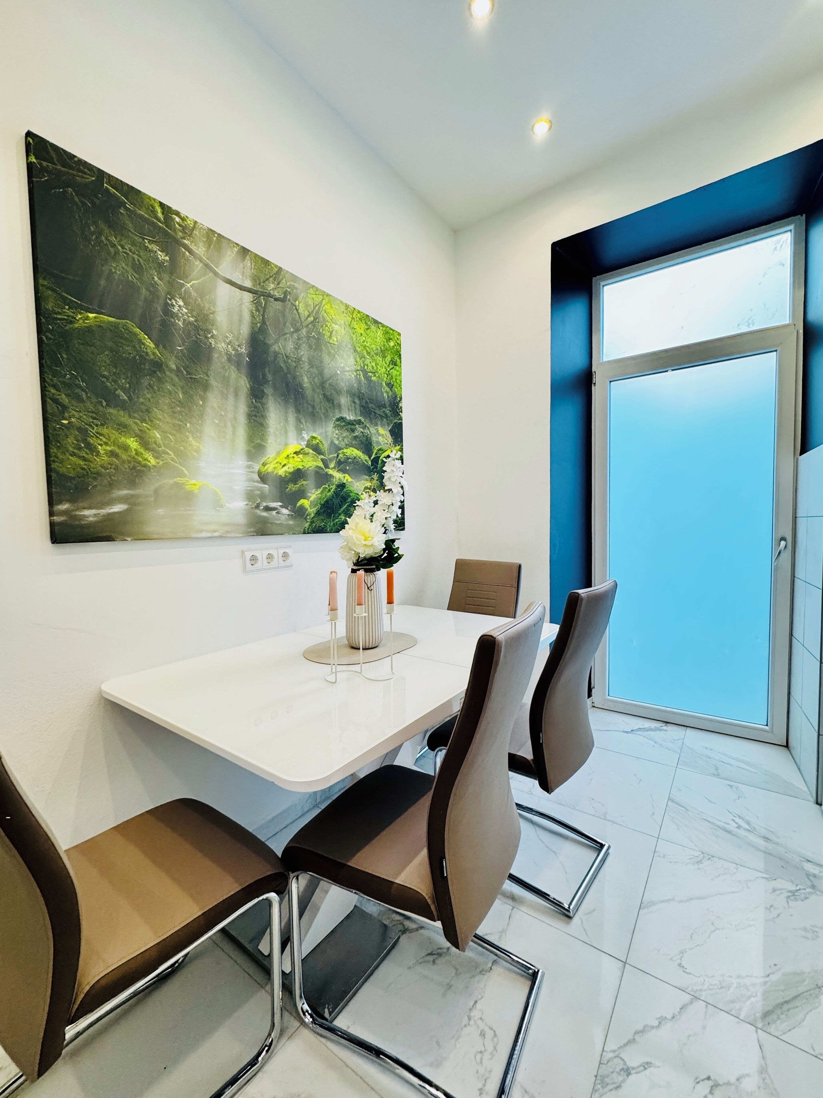 Ein moderner Essbereich mit einem weißen Tisch, braunen Stühlen und einem großen Wandbild mit Naturmotiven.