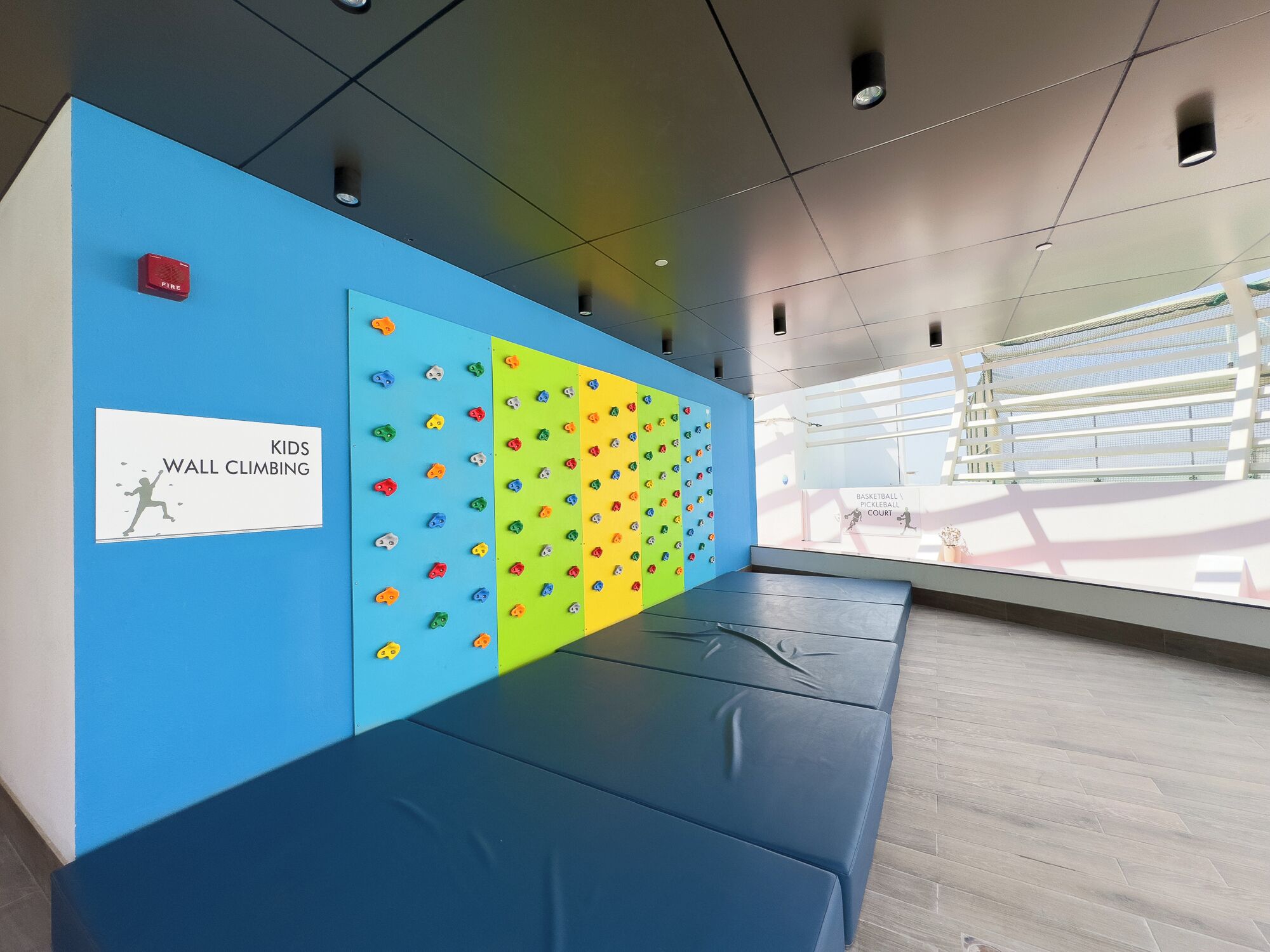 A wall with climbing holds and a sign for kids' wall climbing.