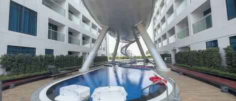 A modern indoor pool with a circular design, surrounded by a wooden deck and a white building with balconies.